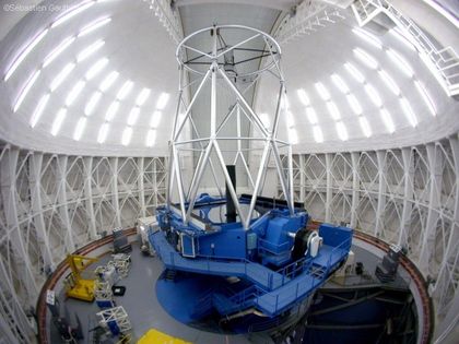 Photo of the interior of an observatory with its dome closed. The walls are white and the base of the telescope is blue.