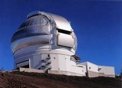 Colour photo of a building with a closed silver and white dome, located on a hill with a blue sky as a backdrop