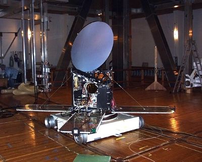 Photo of a white lens and its metal mechanism installed on the wooden floor of a building.