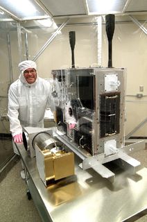 Photo of a man wearing protective clothing pushing a table carrying a rectangular metal box with several assembled components